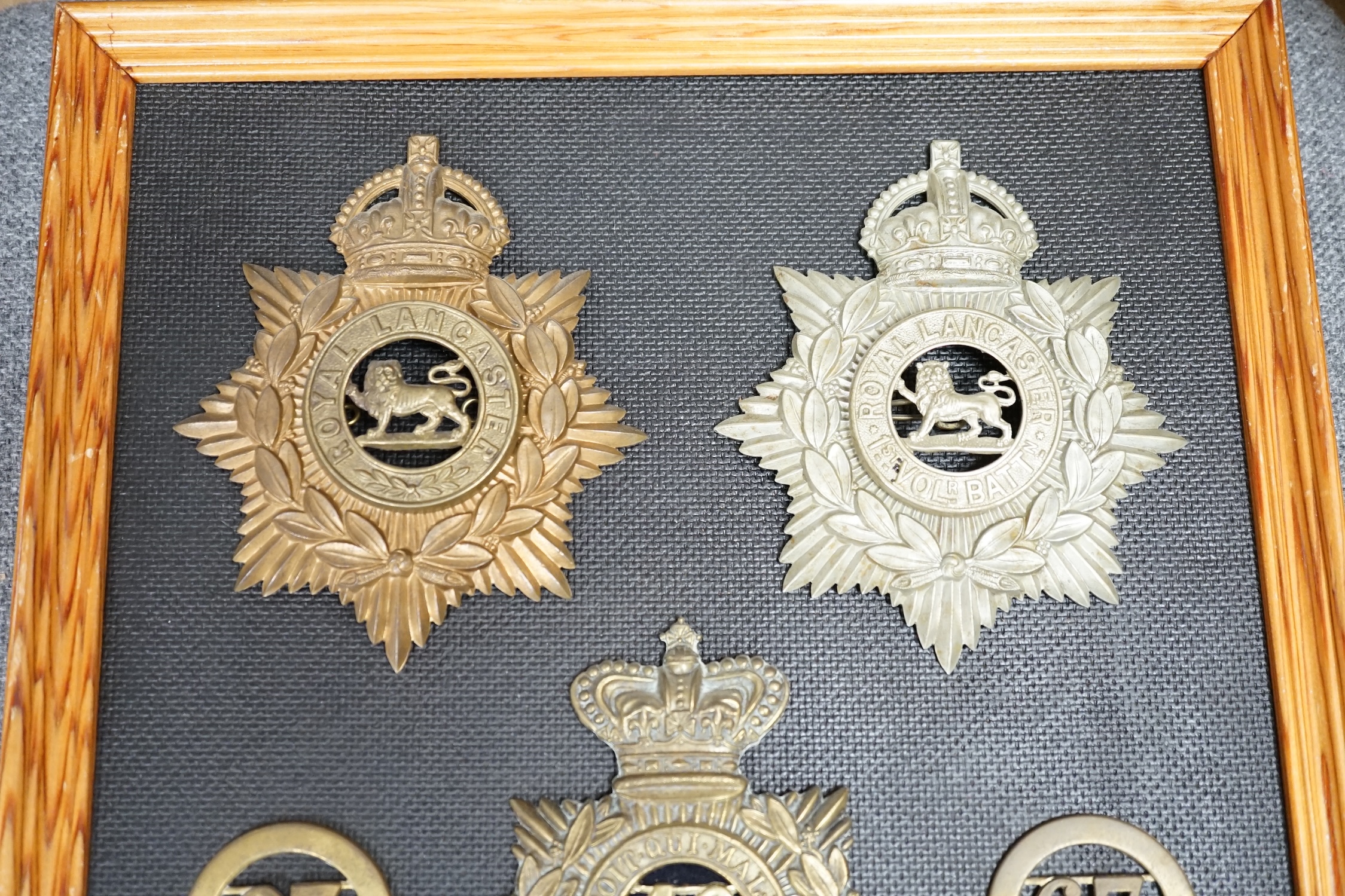 Five military helmet plates and two other centre badges mounted on a board, including; the Royal Lancashire Regiment, the Royal Lancashire 1st Volunteer Battalion, the Oxfordshire Regiment, the Royal Sussex Regiment, etc